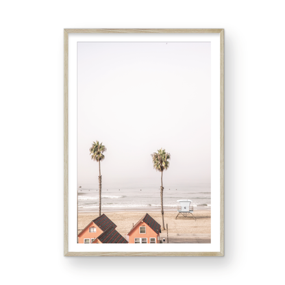 Vertical coastal photography of Oceanside, California, showing beachfront houses and a lifeguard tower with two prominent palm trees overlooking the ocean. A minimalist surf print. Photograph in minimalist mock up.