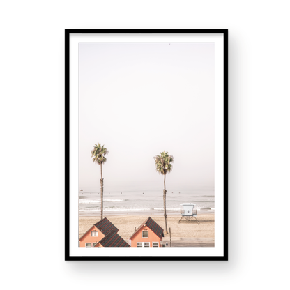 Vertical coastal photography of Oceanside, California, showing beachfront houses and a lifeguard tower with two prominent palm trees overlooking the ocean. A minimalist surf print. Photograph in minimalist mock up.