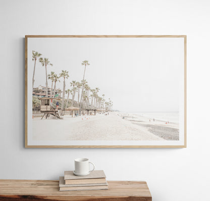 A wide landscape coastal photography view of San Clemente State Beach in Southern California, featuring a row of tall palm trees, a lifeguard tower, and people enjoying the calm beach. This horizontal image evokes Summer Vibes Wall Art and tropical beach print aesthetics. Photograph in minimalist mock up.