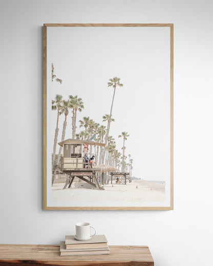 A landscape coastal photography view of San Clemente State Beach in Southern California, featuring a row of tall palm trees, a lifeguard tower, and people enjoying the calm beach. This vertical image evokes Summer Vibes Wall Art and tropical beach print aesthetics. Photograph in minimalist mock up.