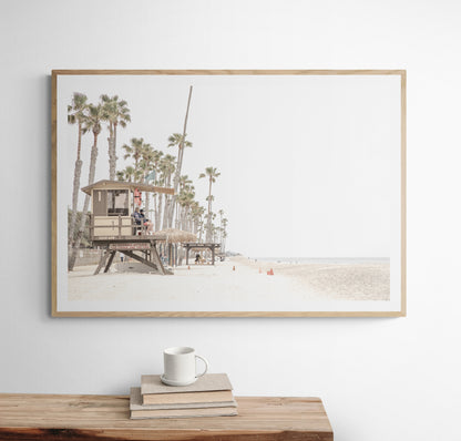 A wide landscape coastal photography view of San Clemente State Beach in Southern California, featuring a row of tall palm trees, a lifeguard tower, and people enjoying the calm beach. This image evokes Summer Vibes Wall Art and tropical beach print aesthetics. Photograph in minimalist mock up.