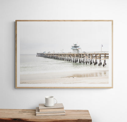 A long wooden pier, the San Clemente Pier, extends into the ocean in this landscape coastal photography. The beach in the foreground suggests a calm ocean print, ideal for a large coastal wall art or a beach cottage wall decor. Photograph in minimalist mock up.