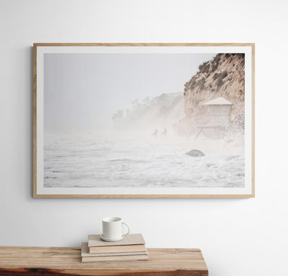 Hazy surf art of two surfers running into stormy ocean waves at Moonlight State Beach, with a lifeguard tower and cliff disappearing into the fog. A dramatic seascape print. Photograph in minimalist mock up
