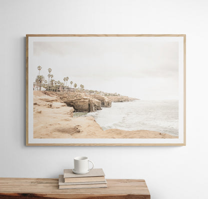 Fine art of Sunset Cliffs, San Diego California horizontal print of hazy high-angle landscape beach photography captures a light blue ocean meeting tall tan, brown cliffs rise as iconic coastal scenery. Photograph in minimalist mock up.