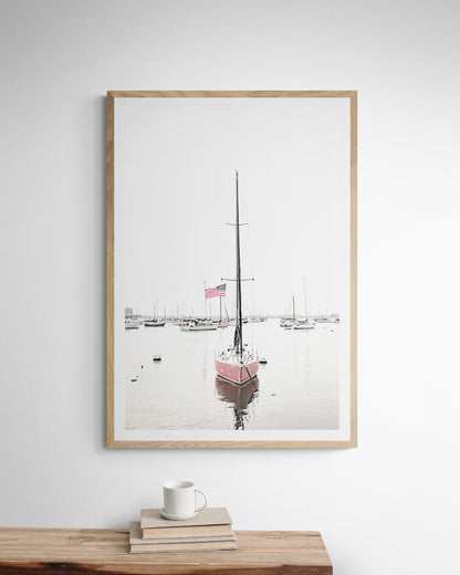 A vertical San Diego print featuring a lone red sailboat with an American flag, anchored in a calm San Diego harbor. This minimalist ocean print captures the essence of coastal photography and is perfect for modern coastal decor. Photograph in minimalist mock up.