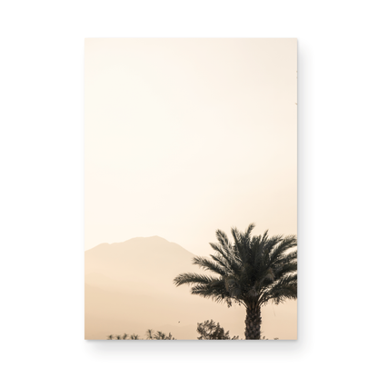 Vertical coastal print of a single palm tree silhouetted against a hazy sky with a distant mountain range, creating a calm beach print feel. Photograph in minimalist mock up.