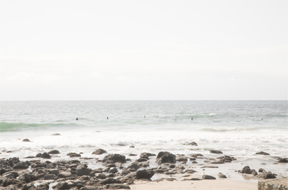 Landscape coastal photography of Salt Creek Beach with dark rocks on the shore and numerous surfers in the ocean. A neutral ocean print perfect for beach house decor. 