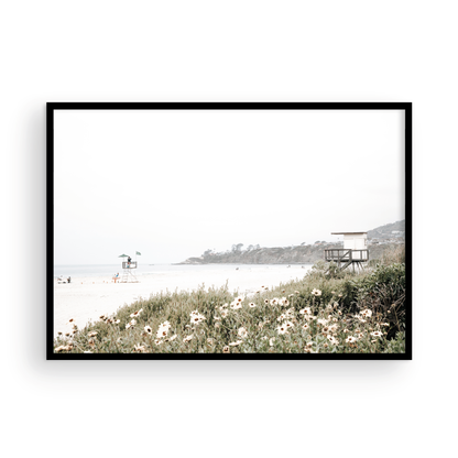 Landscape coastal photography of Salt Creek Beach Park, featuring a lifeguard tower and white flowers in the foreground, with distant cliffs. This calm beach print offers a serene coastal vibe. Photograph in minimalist mock up.