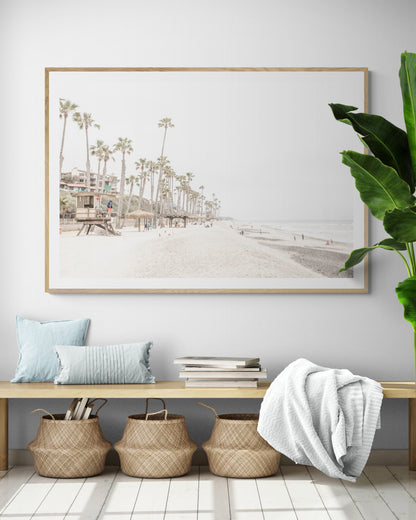 A wide landscape coastal photography view of San Clemente State Beach in Southern California, featuring a row of tall palm trees, a lifeguard tower, and people enjoying the calm beach. This horizontal image evokes Summer Vibes Wall Art and tropical beach print aesthetics. Photograph in minimalist mock up.