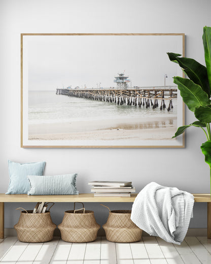 A long wooden pier, the San Clemente Pier, extends into the ocean in this landscape coastal photography. The beach in the foreground suggests a calm ocean print, ideal for a large coastal wall art or a beach cottage wall decor. Photograph in minimalist mock up.