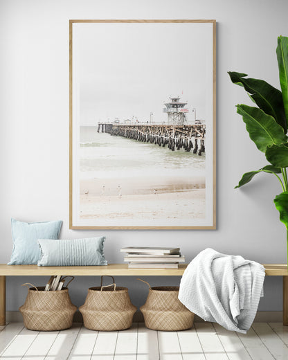 A long wooden pier, the San Clemente Pier, extends into the ocean in this vertical coastal photography. The beach in the foreground suggests a calm ocean print, ideal for a large coastal wall art or a beach cottage wall decor. Photograph in minimalist mock up.