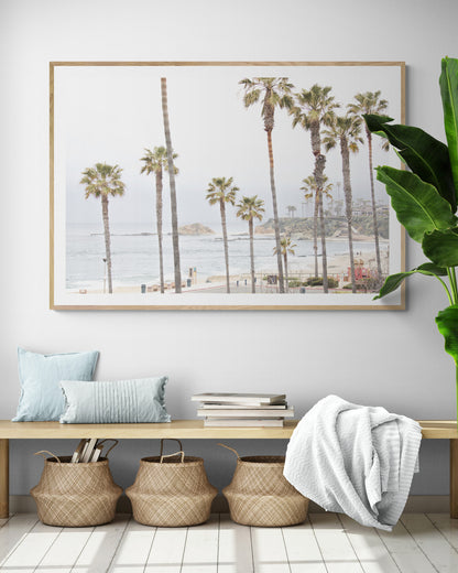 Horizontal coastal photography of a beachscape at Laguna Beach, California, beach art print featuring palm trees and a clear blue sky with a few clouds over a beach scene. Photograph in minimalist mock up.