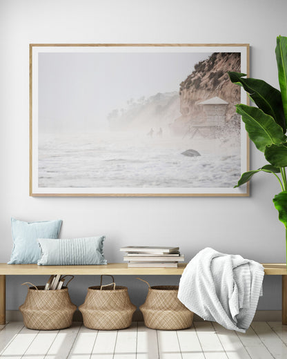 Hazy surf art of two surfers running into stormy ocean waves at Moonlight State Beach, with a lifeguard tower and cliff disappearing into the fog. A dramatic seascape print. Photograph in minimalist mock up