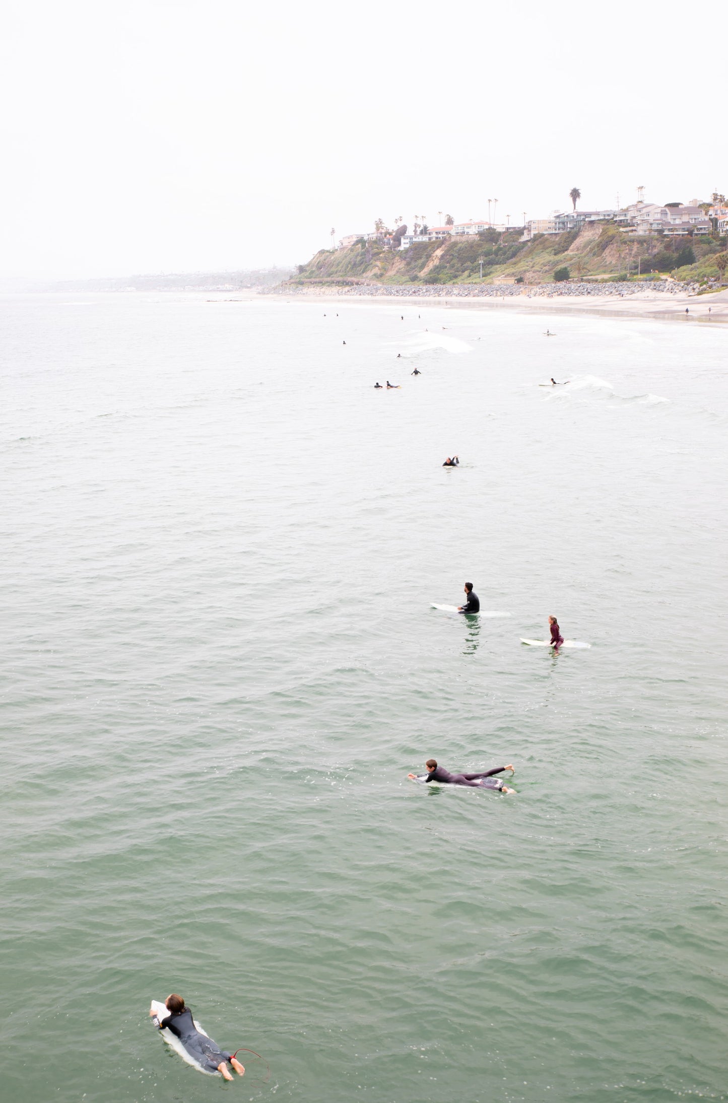 Photography by Kim Dybczak of: Surfers paddle out at California as waves rise and fold toward the beach.