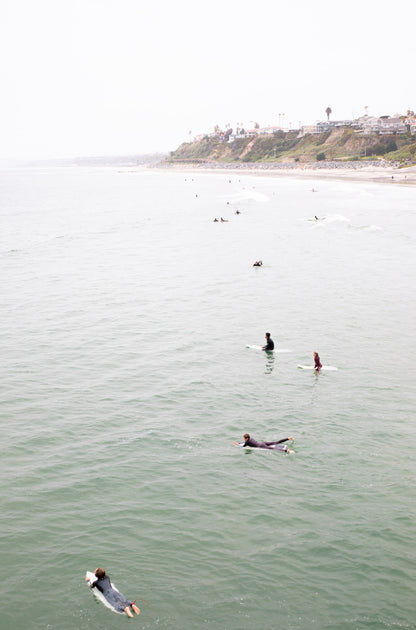 Photography by Kim Dybczak of: Surfers paddle out at California as waves rise and fold toward the beach.