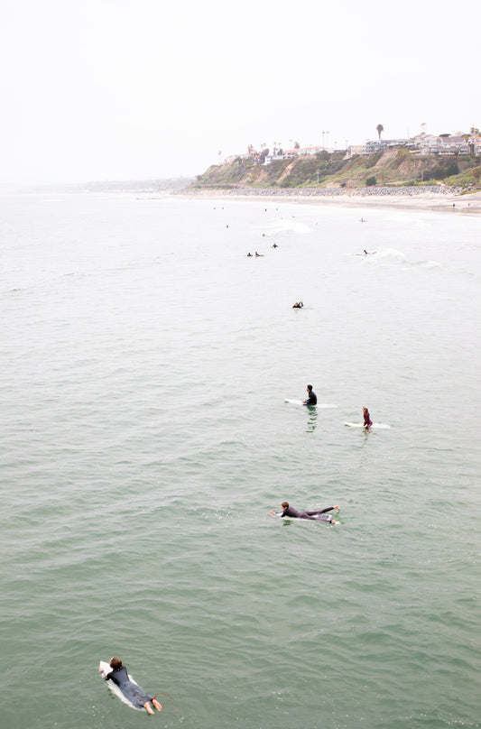 Photography by Kim Dybczak of: Surfers paddle out at California as waves rise and fold toward the beach.