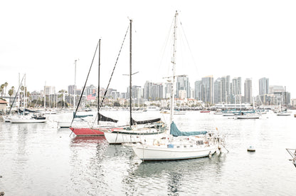 Photography by Kim Dybczak of: A sailboat drifts offshore at San Diego, framed by wide sky and calm water.