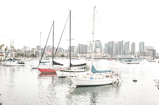 Photography by Kim Dybczak of: A sailboat drifts offshore at San Diego, framed by wide sky and calm water.