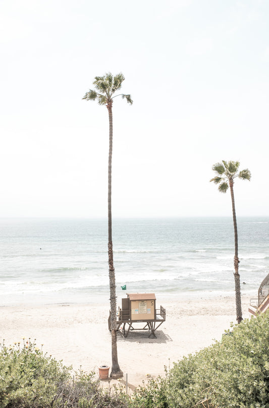 Photography by Kim Dybczak of: California lifeguard tower stands near the shoreline, framed by sand and quiet surf.