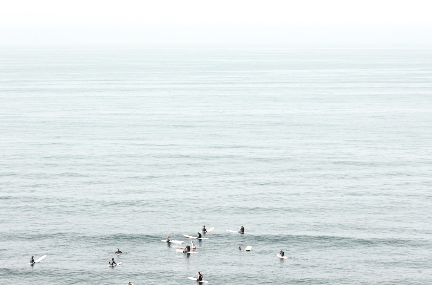 Photography by Kim Dybczak of: Surfers gather offshore at California, spaced out on the calm lineup.