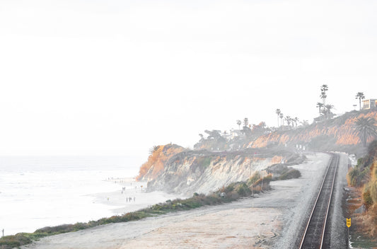 Photography by Kim Dybczak of: Curving train tracks hug a San Diego coastal cliff above a sandy beach and blue water.