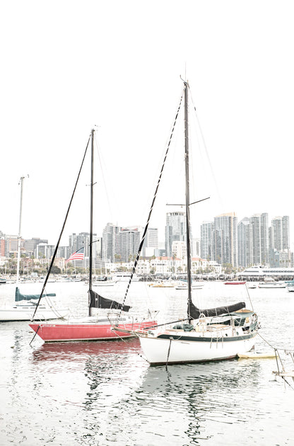 Photography by Kim Dybczak of: A sailboat drifts offshore at San Diego, framed by wide sky and calm water.