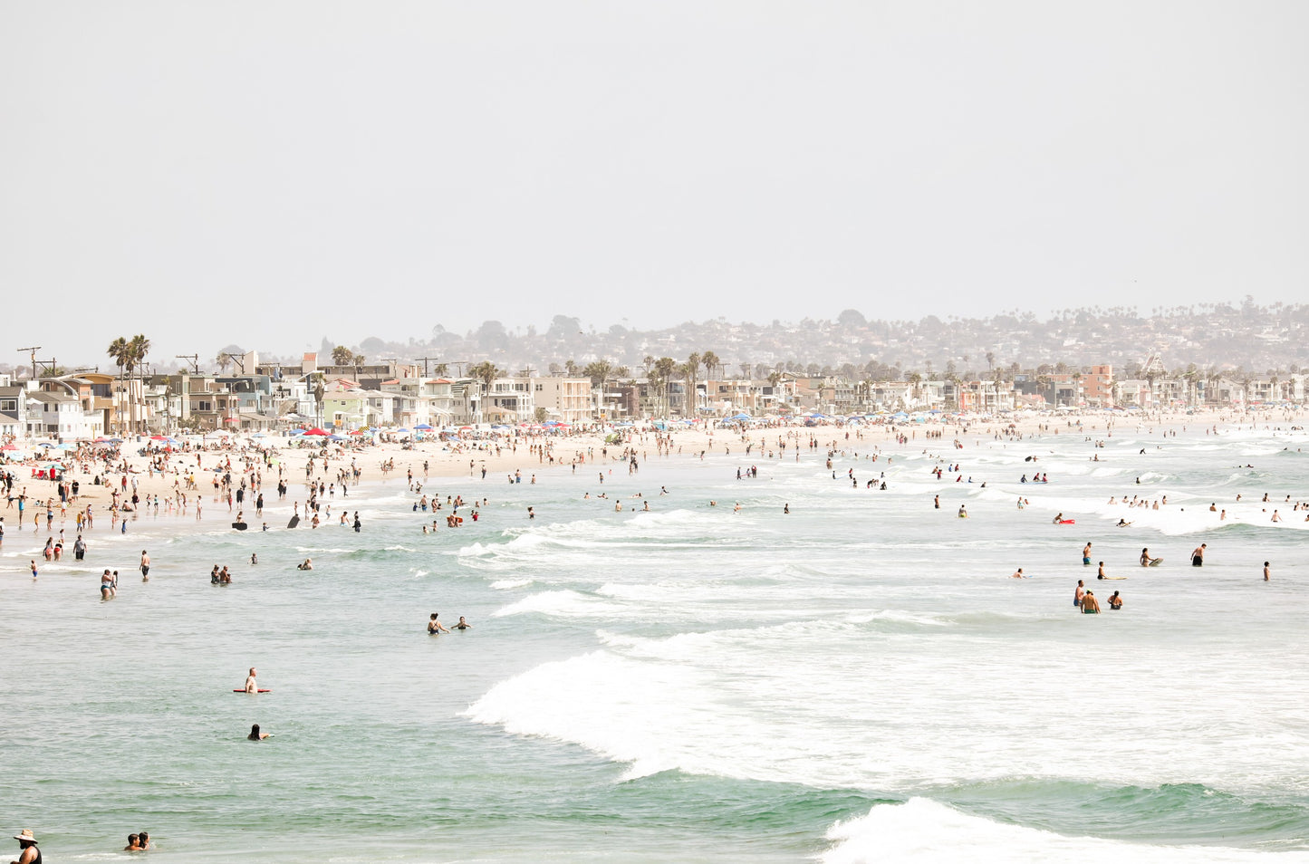 Photography by Kim Dybczak of: A busy public beach in San Diego fills with people along the shoreline and in the water.