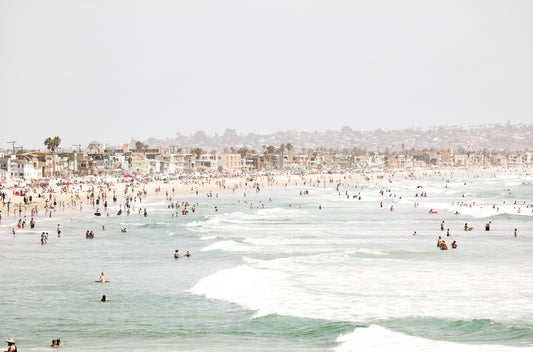 Photography by Kim Dybczak of: A busy public beach in San Diego fills with people along the shoreline and in the water.
