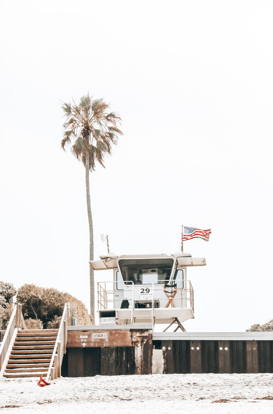Photography by Kim Dybczak of: A simple lifeguard tower stands on the sand at Del Mar, with gentle waves behind it.
