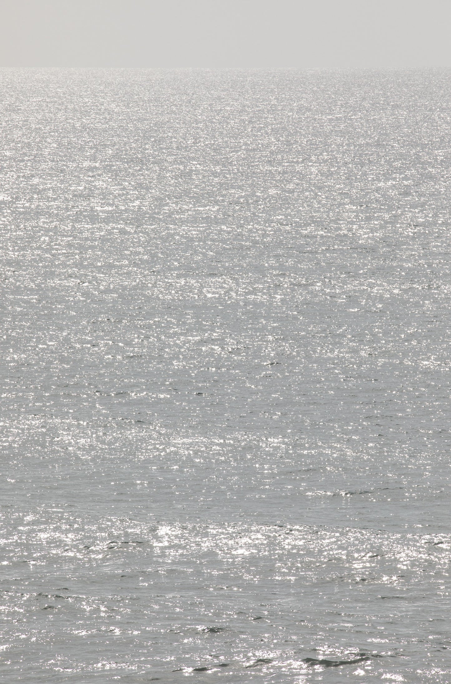 Photography by Kim Dybczak of: Sunlight sparkles across a bright ocean surface in a vertical seascape.