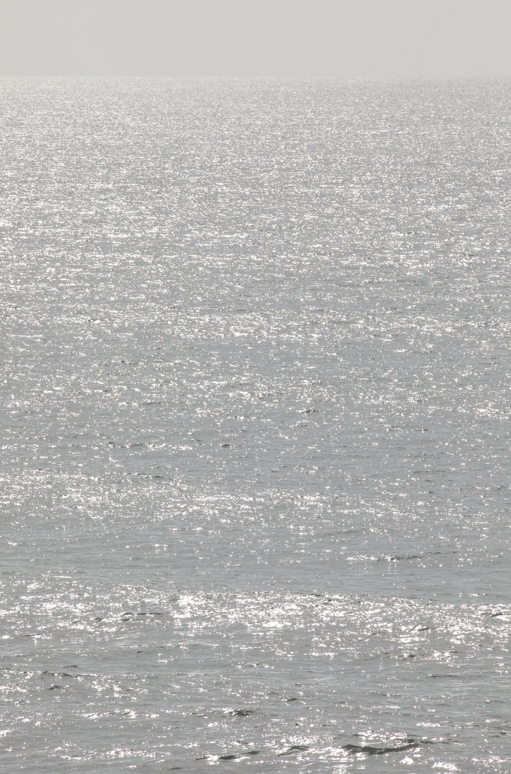 Photography by Kim Dybczak of: Sunlight sparkles across a bright ocean surface in a vertical seascape.