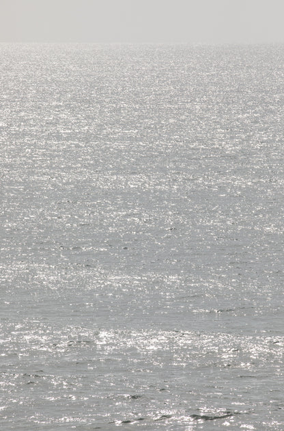 Photography by Kim Dybczak of: Sunlight sparkles across a bright ocean surface in a vertical seascape.