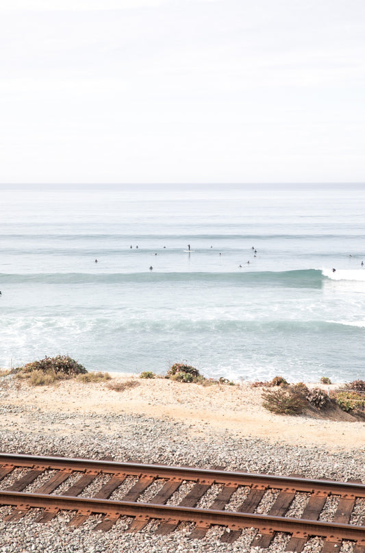 Photography by Kim Dybczak of: Waves and surfers appear near train tracks along the coast in Del Mar, San Diego.