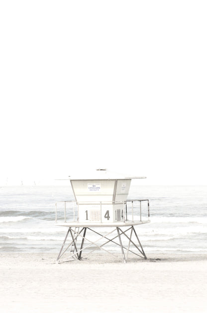 Photography by Kim Dybczak of: A pale lifeguard tower stands near the shore with ocean waves in the distance.