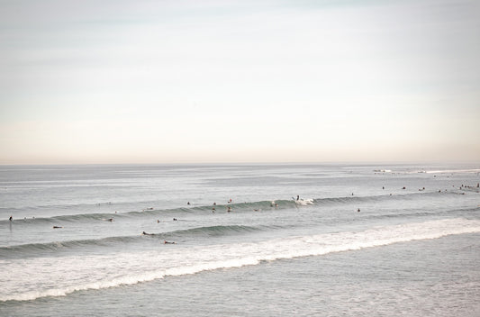 Photography by Kim Dybczak of: Surfers paddle out at Pacific Beach as waves rise and fold toward the beach.
