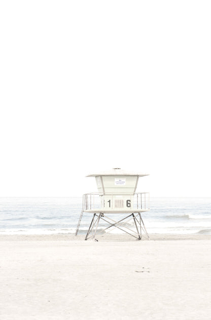 Photography by Kim Dybczak of: A pale lifeguard tower stands near the shore with ocean waves in the distance.