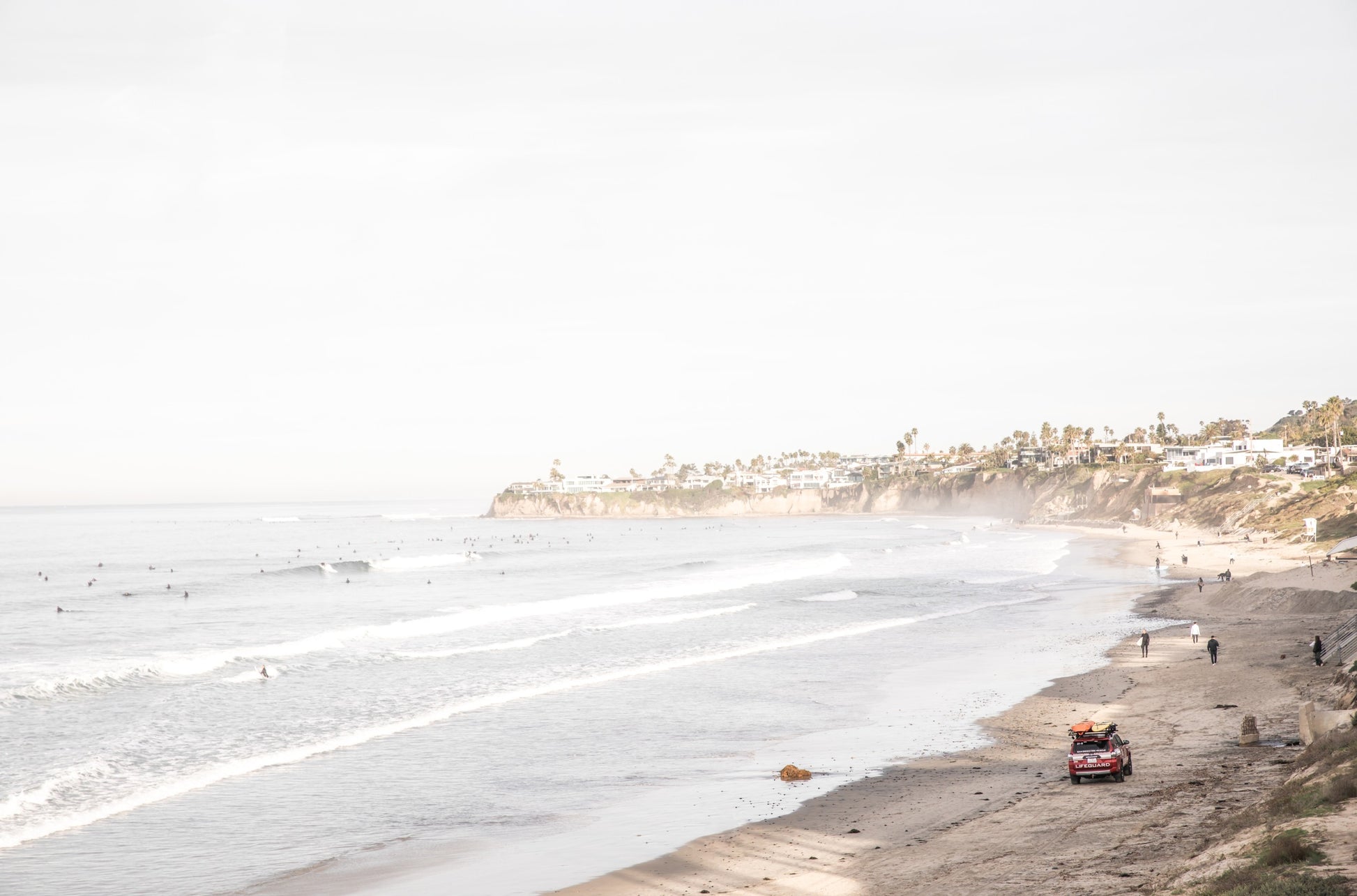 Photography by Kim Dybczak of: Surfers gather offshore at Pacific Beach below a residential cliffside in San Diego.