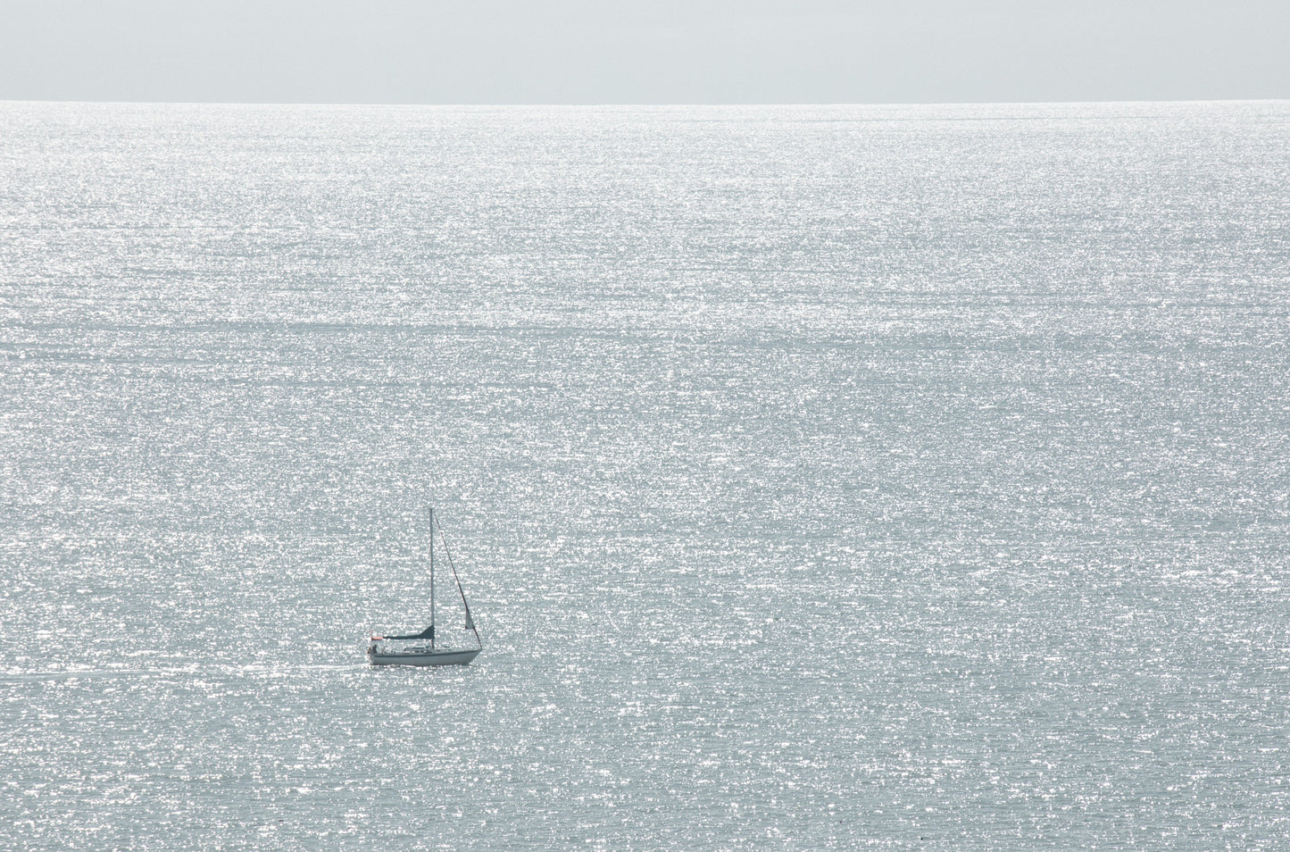Photography by Kim Dybczak of: A lone sailboat glides on open water near San Diego, standing out against the sea.