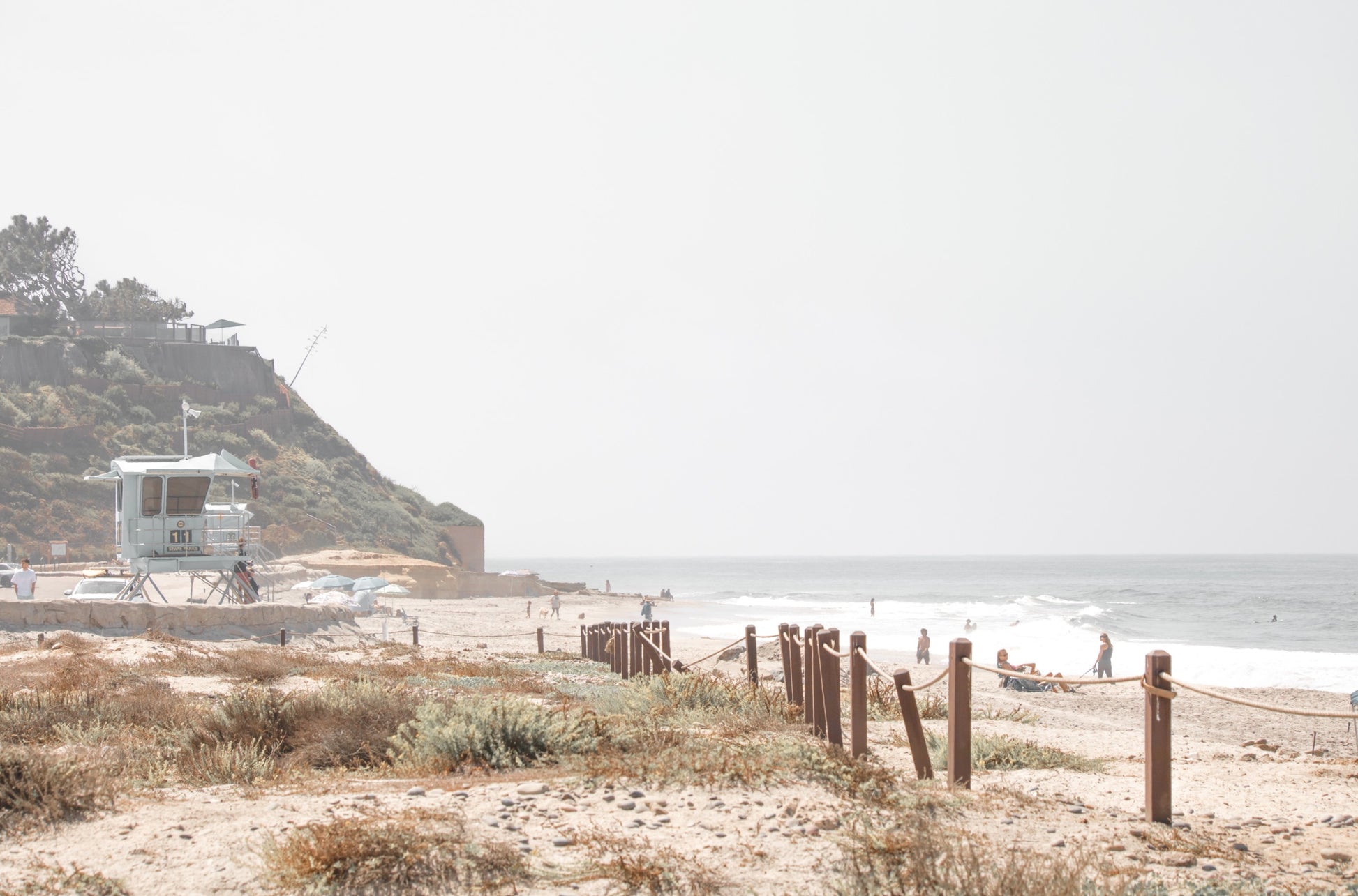Photography by Kim Dybczak of: California lifeguard tower stands near the shoreline, framed by sand and quiet surf.