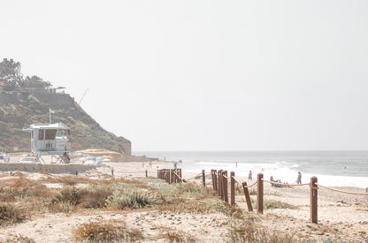 Photography by Kim Dybczak of: California lifeguard tower stands near the shoreline, framed by sand and quiet surf.