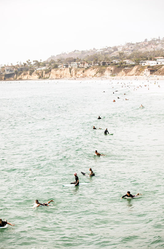 Photography by Kim Dybczak of: Surfers paddle out at Pacific Beach as waves rise and fold toward the beach.
