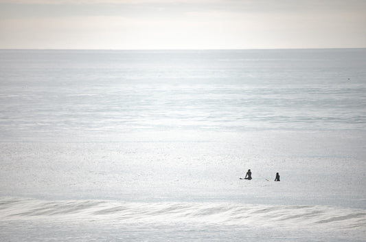 Photography by Kim Dybczak of: Surfers paddle out as waves rise and fold toward the beach.