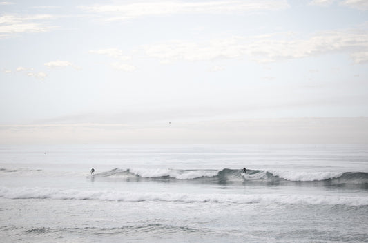 Photography by Kim Dybczak of: Surfers paddle out as waves rise and fold toward the beach.