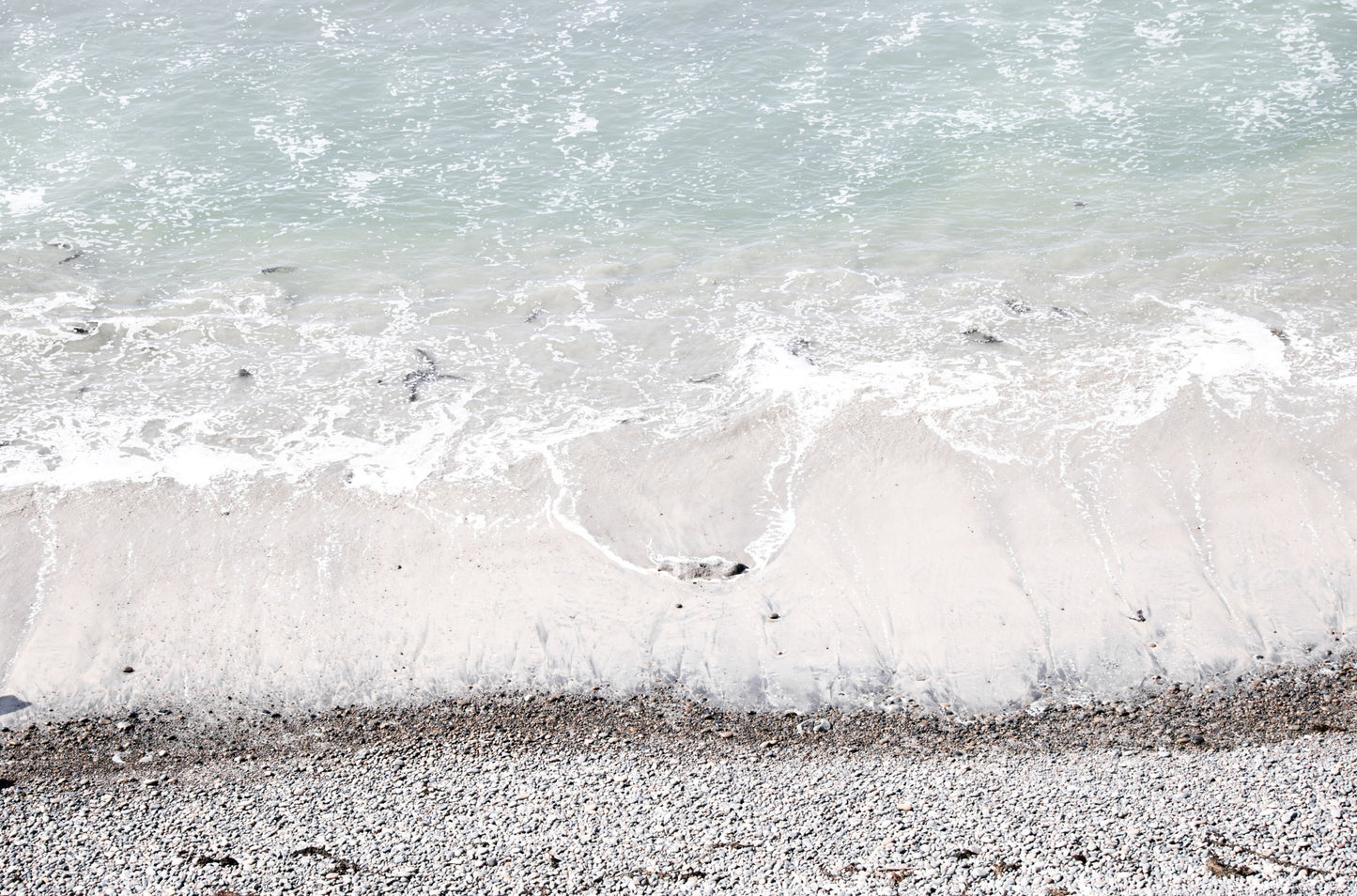 Photography by Kim Dybczak of: A rocky shoreline meets foamy waves along a rugged stretch of coast.