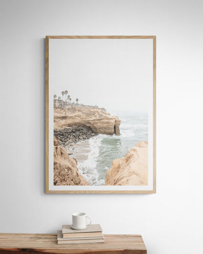 Fine art of Sunset Cliffs, San Diego California vertical print of hazy high-angle landscape beach photography captures a light blue ocean meeting tall tan, rocky, brown cliffs rise as iconic coastal scenery. Photograph in minimalist mock up.