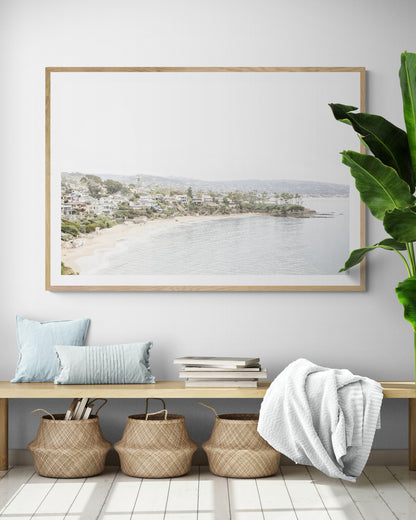 Horizontal coastal photography featuring a beach scene with a calm ocean and beach homes lining the shoreline, located in Laguna California. Photograph in minimalist mock up.