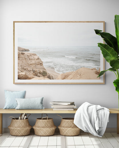 Fine art of Sunset Cliffs, San Diego California horizontal print of hazy high-angle landscape beach photography captures a light blue ocean meeting tall tan and brown cliffs rise as iconic coastal scenery. Photograph in minimalist mock up.