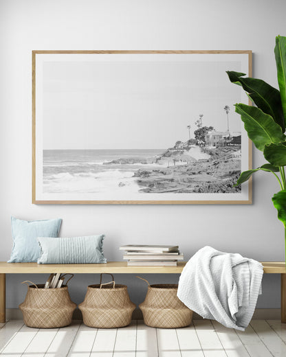 Fine art of WindanSea Beach, La Jolla California horizontal landscape black and white print by Southern California photographer Kim Dybczak of Salt Creek Prints, featuring a powerful waves crashing against the rocky shore of California coast. Beach homes and palm trees sit atop the cliffside, with stairs leading down to a sheltered area. Photograph in minimalist mock up
