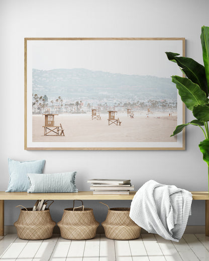 Landscape beach photography of Santa Monica State Beach with multiple lifeguard towers on the vast sandy expanse and hazy hills in the background. Photograph in minimalist mock up
