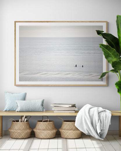 Horizontal minimalist ocean art with a close-up blue waves print of water, featuring subtle ripples and soft textures, ideal as a neutral ocean print, two surfers sit and watch the waves. Photograph in minimalist mock up.